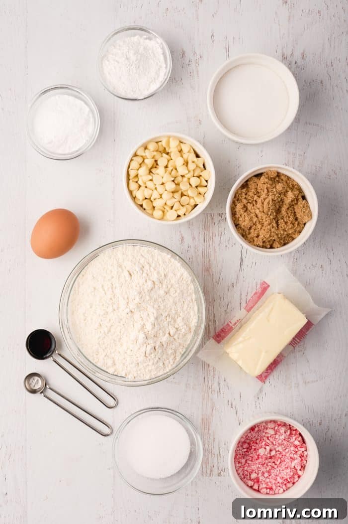 A top-down view of all the ingredients laid out for peppermint white chocolate cookies, including flour, sugars, butter, eggs, extracts, white chocolate chips, and crushed candy canes.