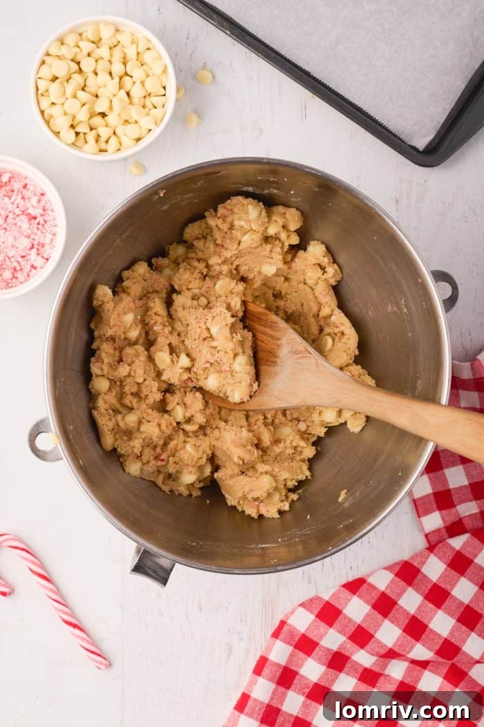 A close-up of cookie dough mixed with white chocolate chips and crushed candy canes, ready for scooping.