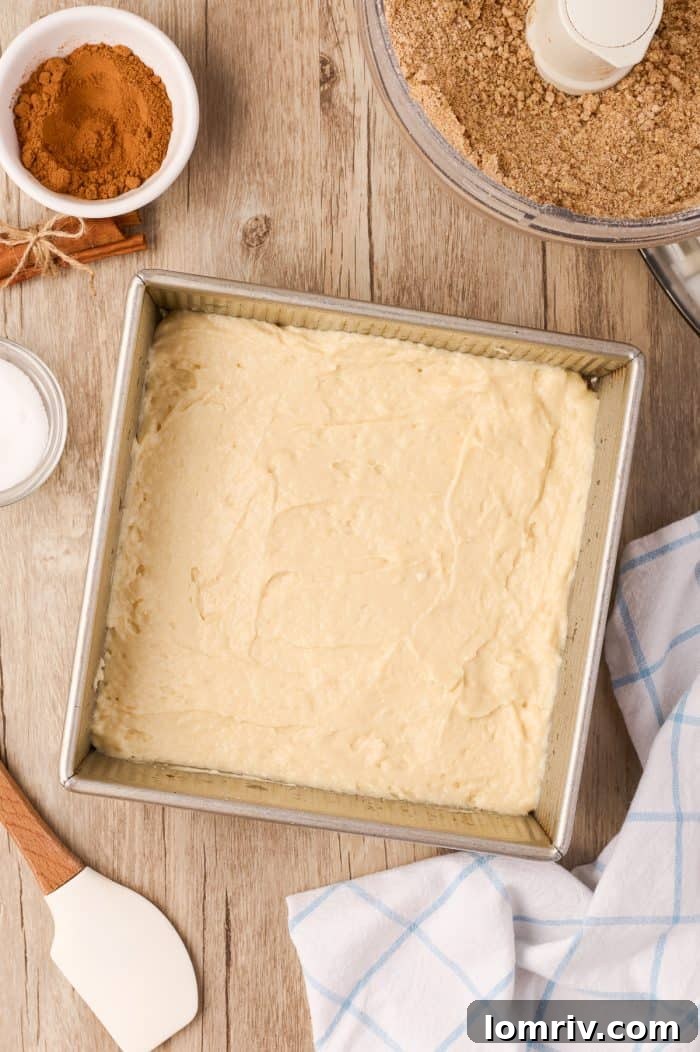 Unbaked sour cream coffee cake in the pan, showing the first layer of batter and streusel.