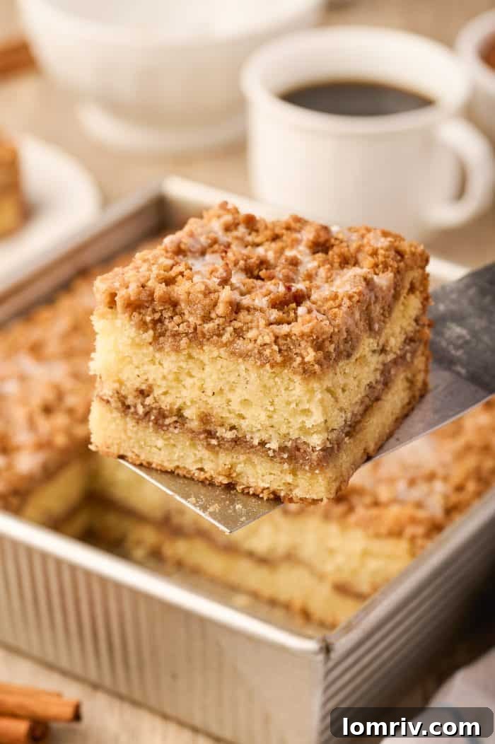 A spatula gently lifting a slice of sour cream coffee cake from the baking pan, highlighting its soft texture.