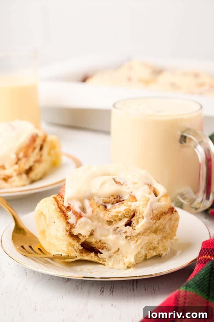 A delectable Eggnog Cinnamon Roll on a plate with a bite taken out, showing its fluffy interior and gooey filling.