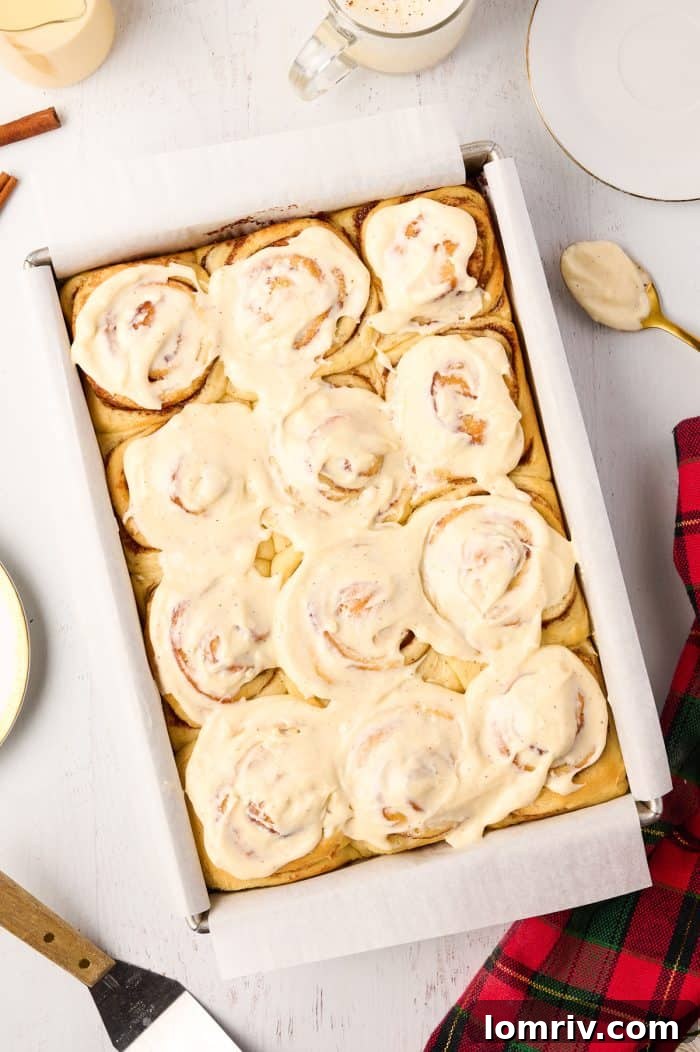 A full pan of golden-brown Eggnog Cinnamon Rolls, generously topped with a decadent layer of white icing.