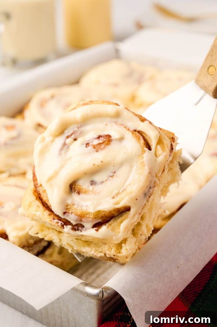 A single Eggnog Cinnamon Roll being carefully lifted from the baking pan, showcasing its perfect swirl and golden-brown crust.