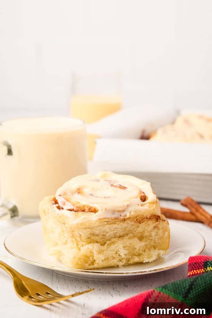 A single, perfectly iced Eggnog Cinnamon Roll on a white plate, ready to be enjoyed.