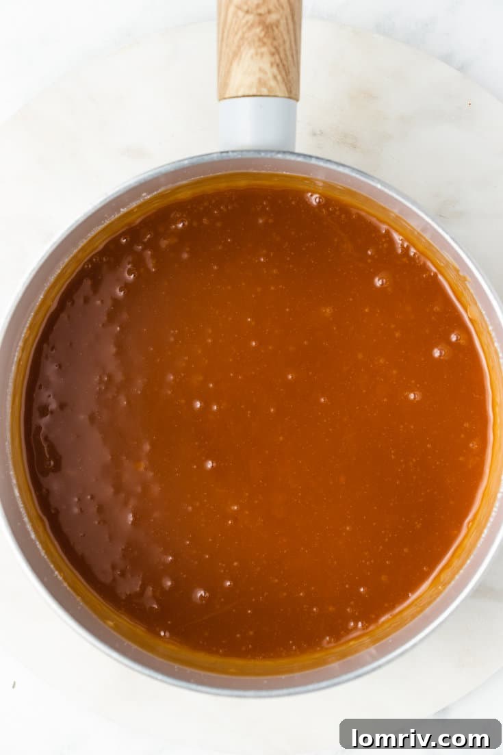 Freshly made caramel sauce, still warm and glossy, being whisked in a saucepan after adding cream, butter, and vanilla.