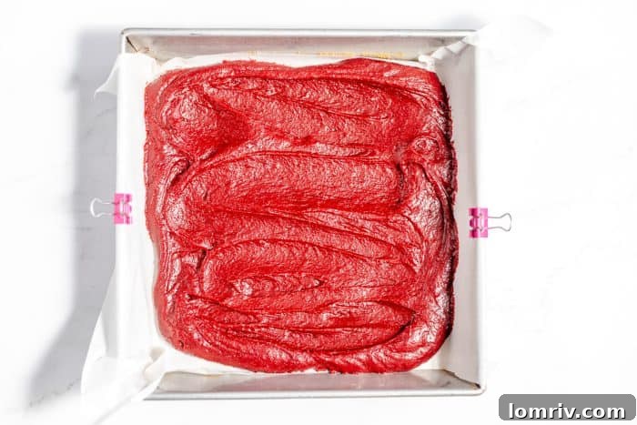 Red velvet brownie batter evenly spread in a prepared baking pan.