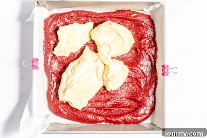 Creamy cheesecake filling poured over the red velvet brownie batter in the baking pan.