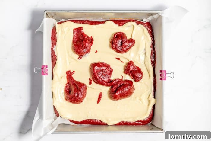 Red velvet brownie batter dotted over cheesecake filling, ready for swirling.