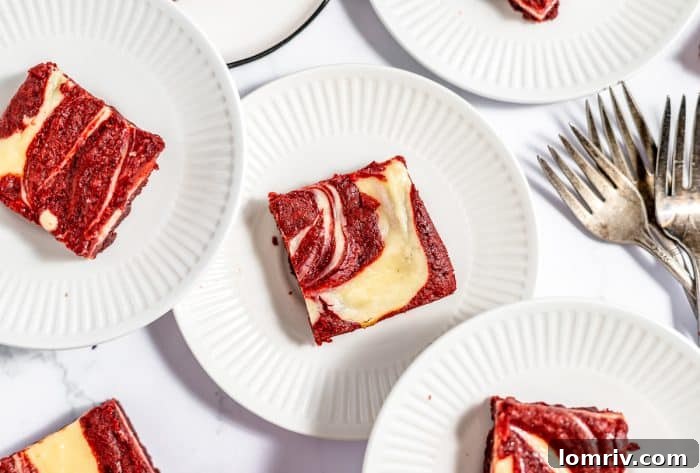 A selection of red velvet cheesecake brownies artfully arranged on white plates, showcasing their beautiful swirled tops.