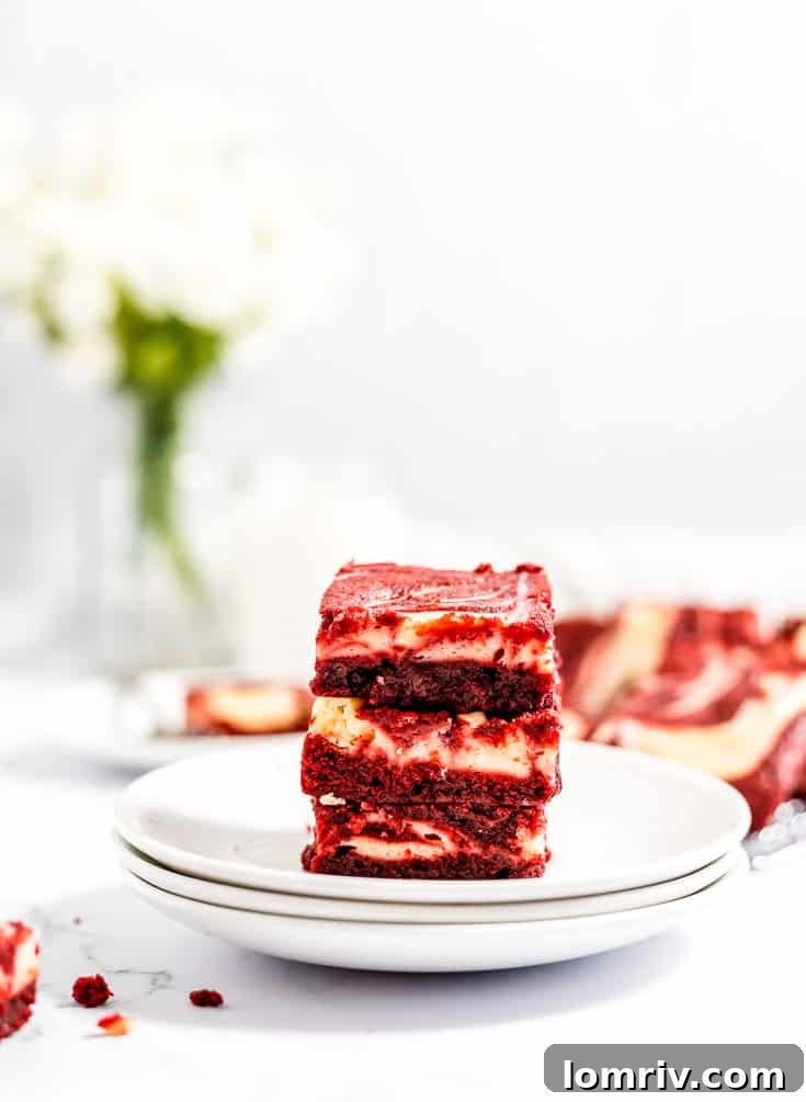 A charming stack of freshly baked red velvet cheesecake brownies presented on white plates, highlighting their enticing layers.
