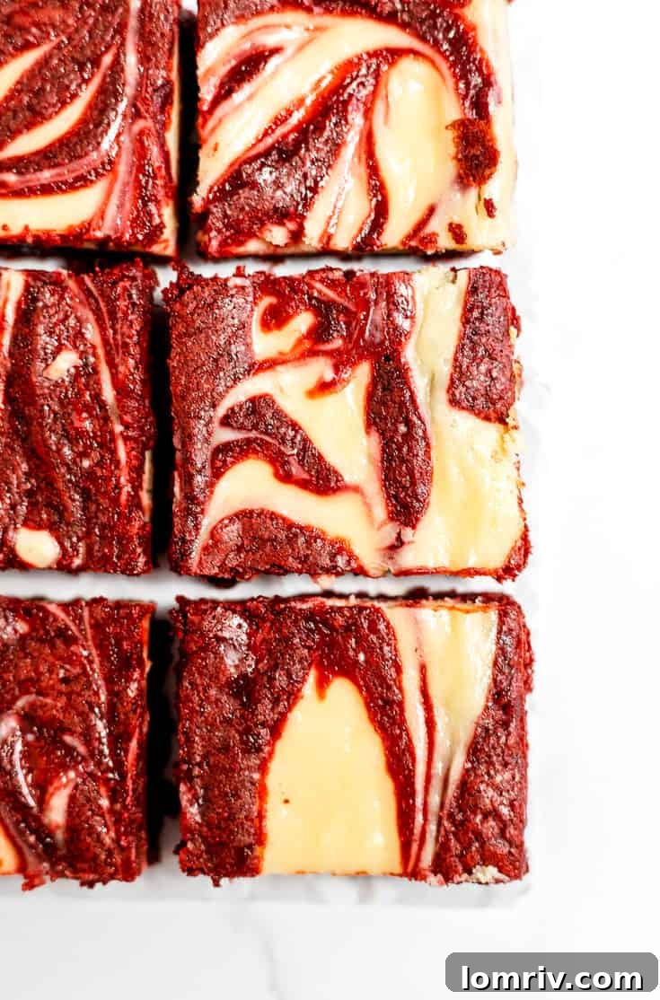 Close-up of perfectly sliced red velvet cheesecake brownies, revealing the distinct red brownie layer and the creamy white cheesecake swirl.