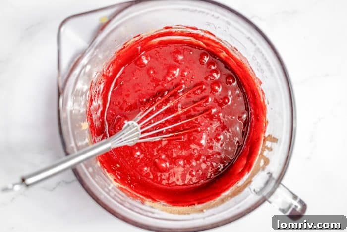 Red velvet brownie batter with melted butter and food coloring being whisked in a bowl.
