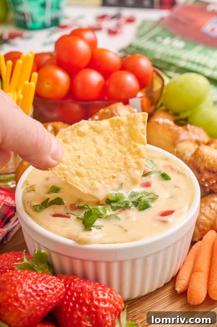 A hand reaching for a tortilla chip, about to dip it into the homemade queso dip on the charcuterie board.