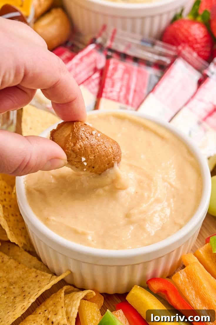 A hand dipping a pretzel bite into the creamy beer cheddar cheese dip, illustrating its perfect consistency.