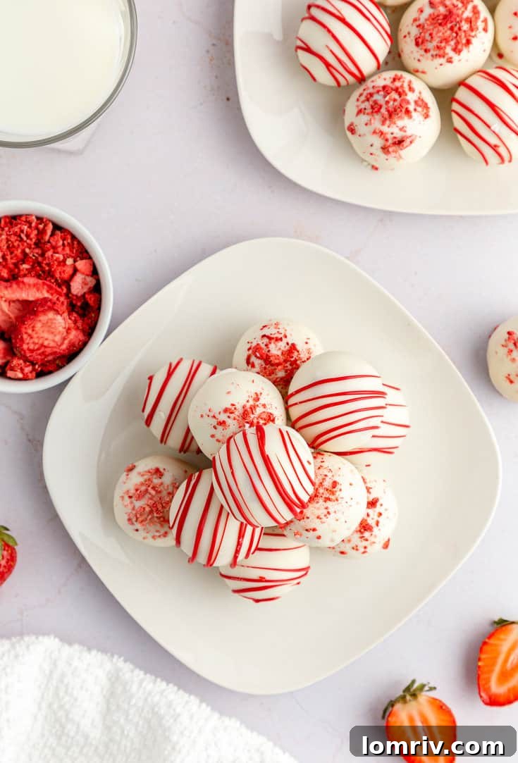 A close-up of beautifully presented strawberry cake balls, adorned with white and red chocolate drizzles and strawberry crumbs.