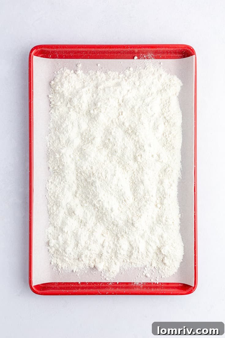 A baking sheet with vanilla cake mix spread evenly, prepared for heat treatment in the oven.