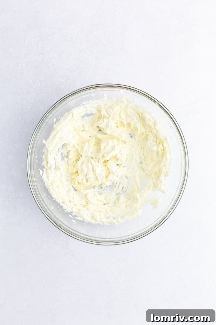 Softened cream cheese being beaten in a medium mixing bowl, appearing smooth and creamy.