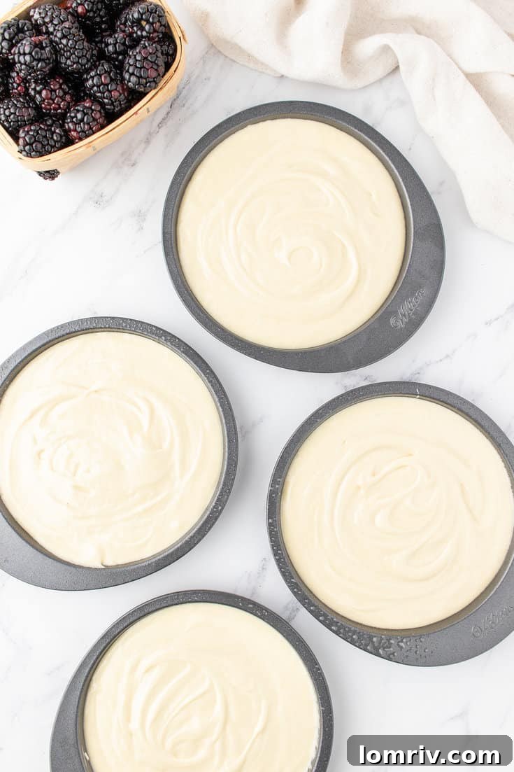 Cake batter evenly divided into four round cake pans, ready for the oven.