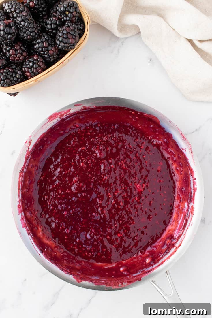 Blackberry puree simmering in a saucepan on the stovetop, thickening into a jam.