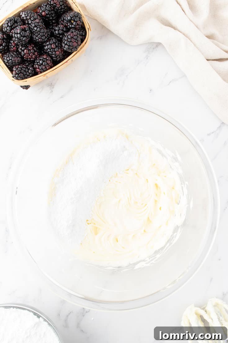 Powdered sugar being gradually added to creamed butter in a mixing bowl for buttercream.