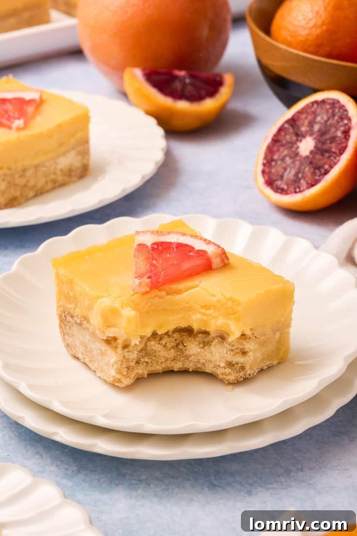 A grapefruit bar with a bite out of it on stacked white plates.