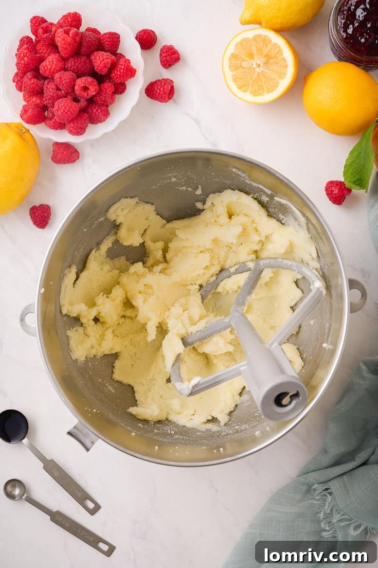 Creaming softened unsalted butter in an electric mixer using the paddle attachment, creating a pale, fluffy, and voluminous base for the raspberry buttercream.