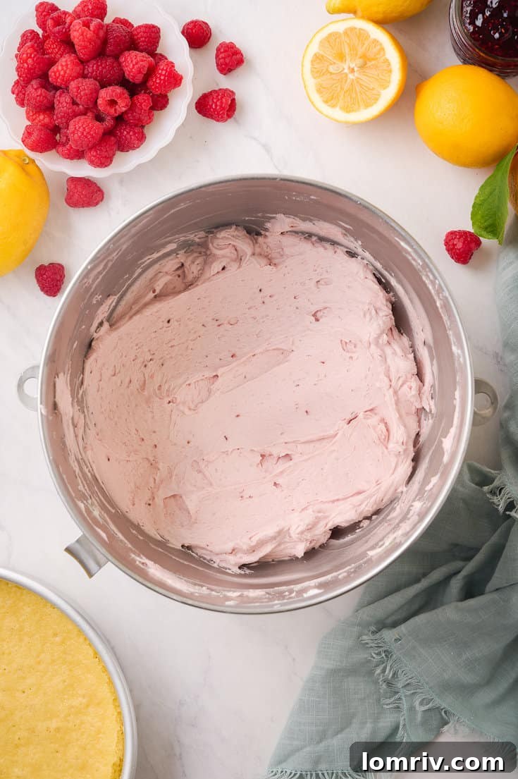 All ingredients for the raspberry buttercream frosting, including powdered sugar, vanilla, heavy cream, salt, and raspberry compote, being mixed into the creamed butter in a stand mixer.