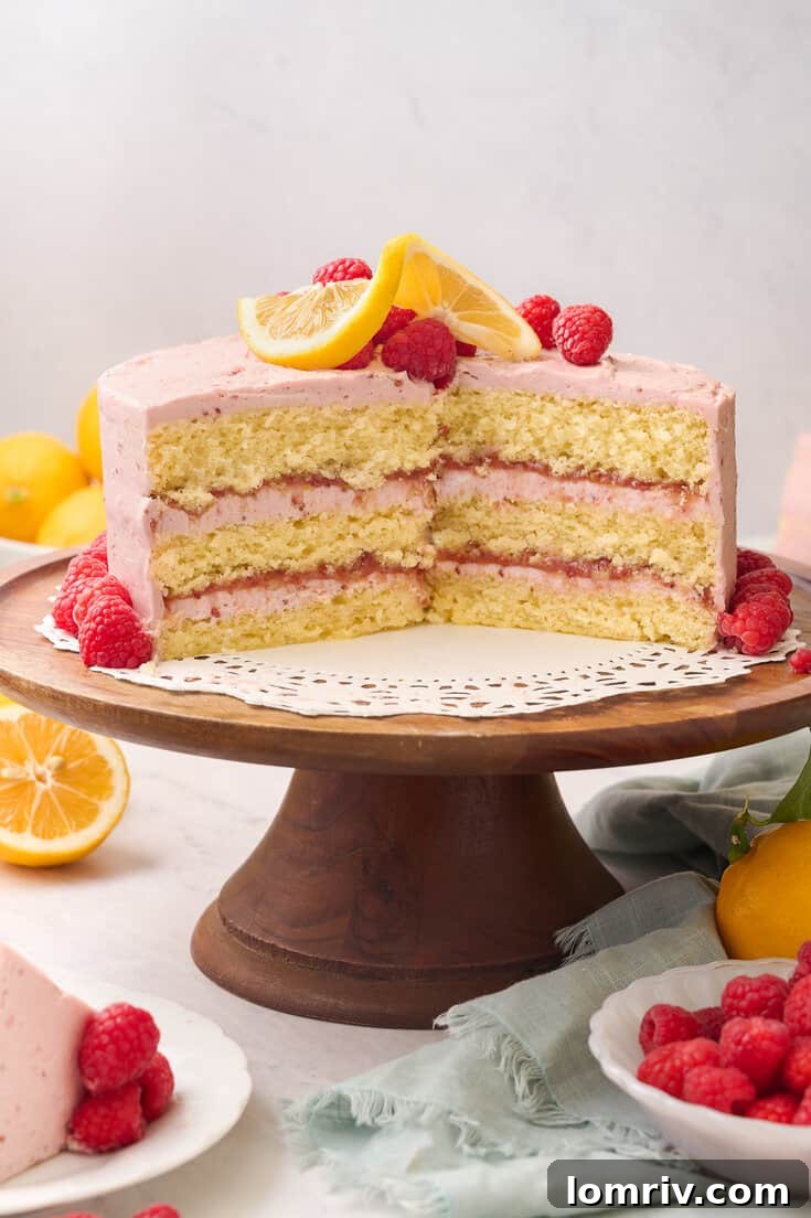 A beautiful cross-section of the Lemon Raspberry Layer Cake displayed on a cake stand, highlighting the contrasting colors and textures of the lemon cake, curd, and raspberry buttercream.