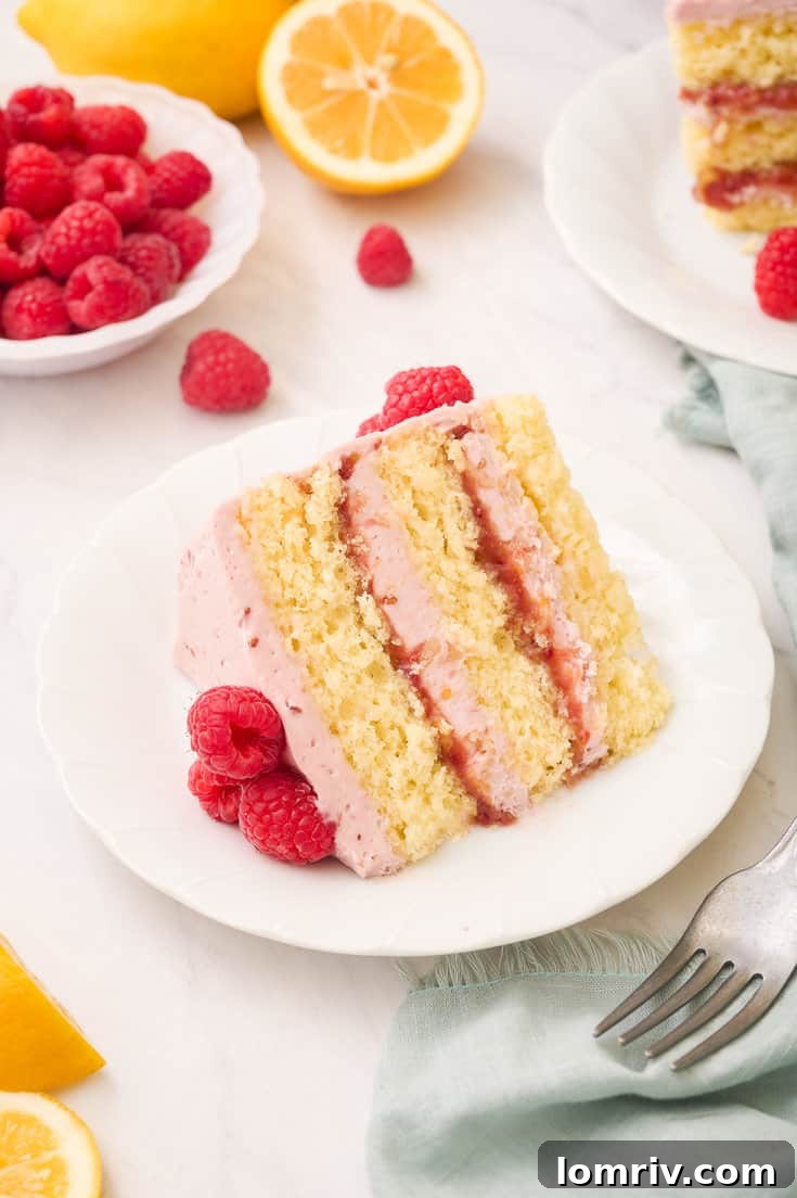 A perfectly sliced piece of Lemon Raspberry Layer Cake, revealing its moist lemon cake layers, creamy homemade lemon curd, and vibrant raspberry filling, topped with smooth raspberry buttercream.