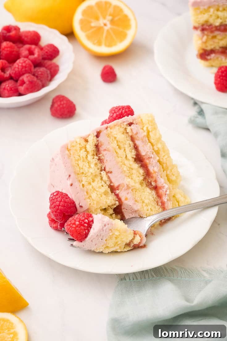 A close-up of a delectable slice of Lemon Raspberry Layer Cake, showing the airy cake crumb and the luscious, creamy filling and frosting in exquisite detail.