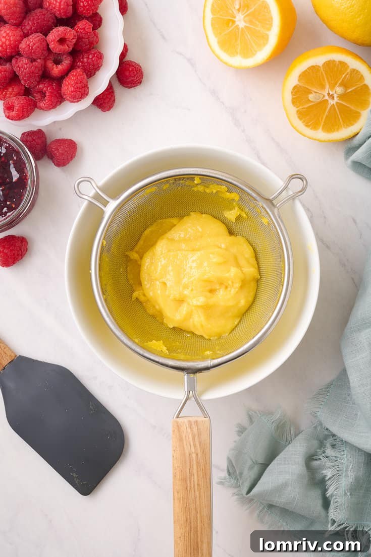 The finished lemon curd being carefully strained through a fine sieve into a small glass bowl, ensuring a perfectly smooth consistency, before combining with raspberry preserve.