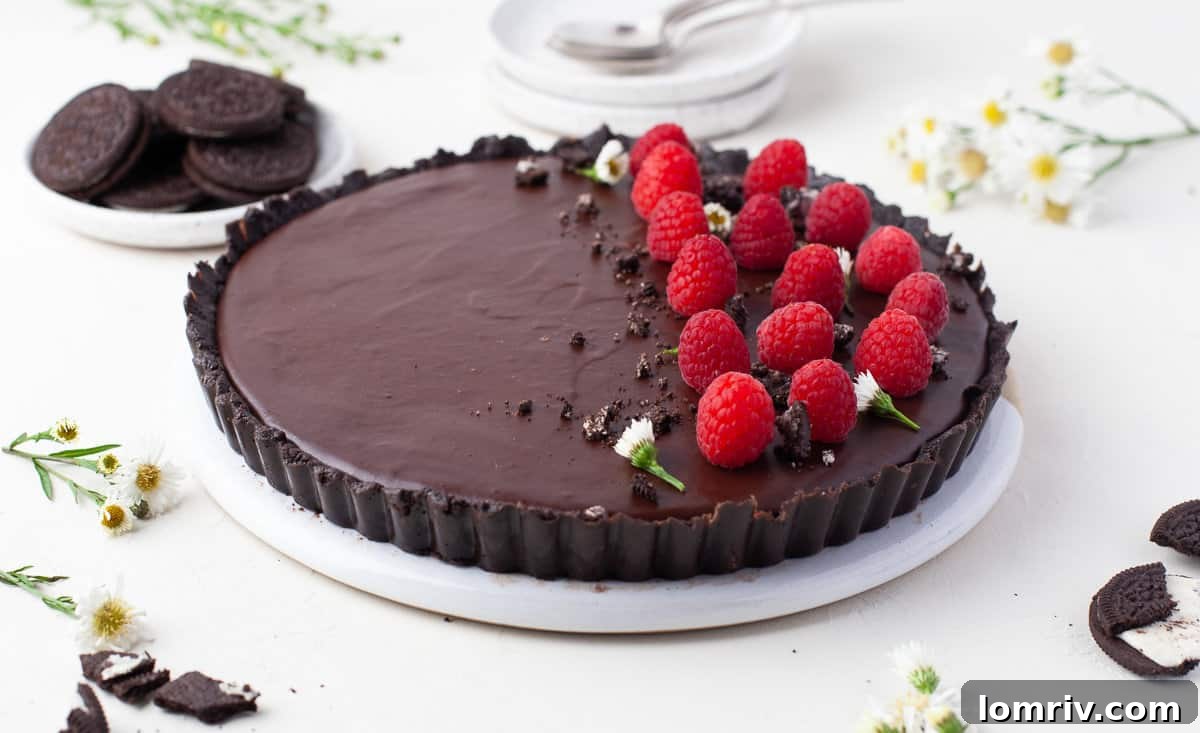 A stunning no-bake chocolate tart garnished with fresh raspberries, cocoa powder, and sea salt, ready to be sliced