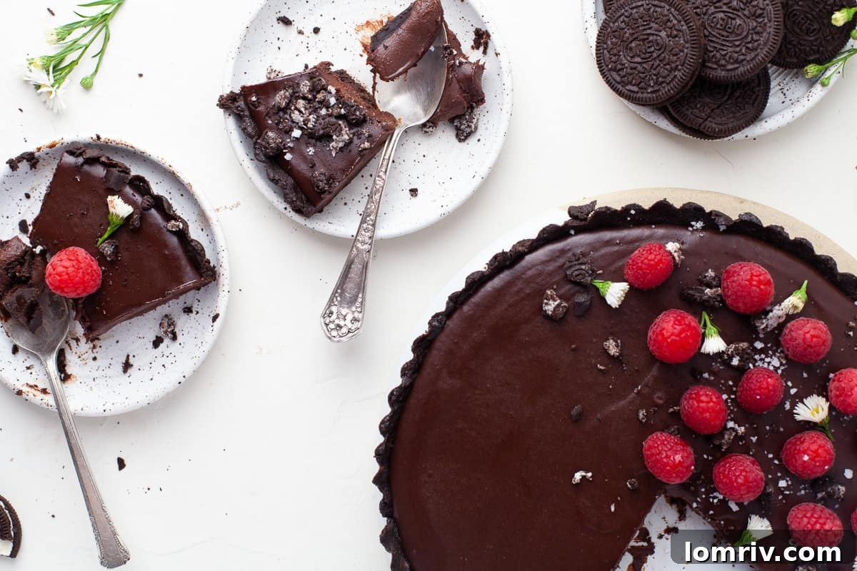 Three slices of no-bake chocolate tart on plates, garnished with fresh raspberries and cocoa
