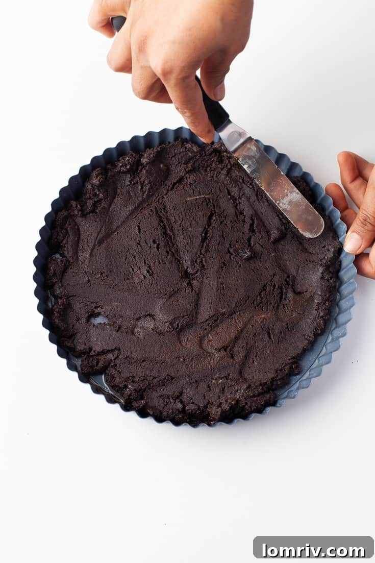 Firmly pressing the Oreo crust mixture into a tart pan
