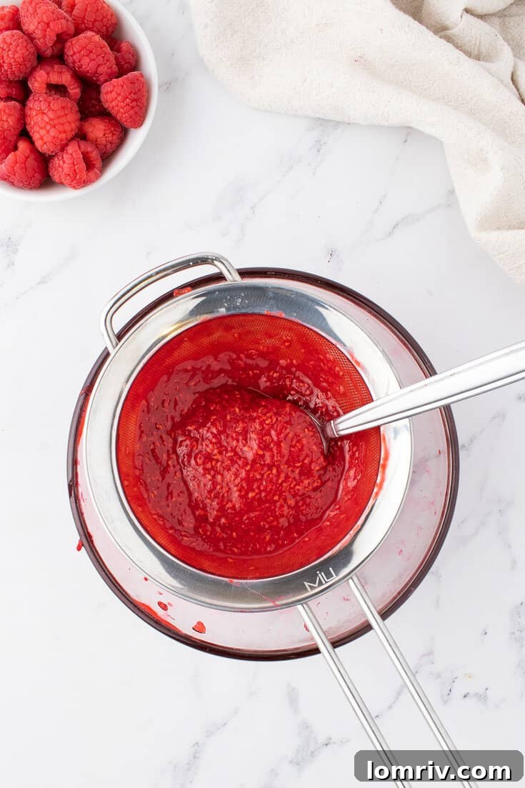 Straining raspberry puree through a fine-mesh sieve to remove seeds