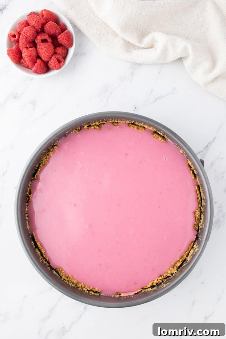 Pouring the smooth raspberry white chocolate ganache over the chilled cheesecake