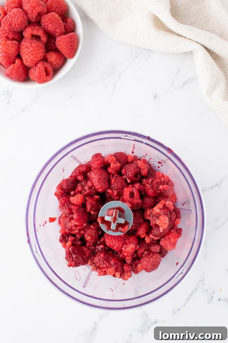 Blending frozen raspberries in a food processor to create a smooth puree