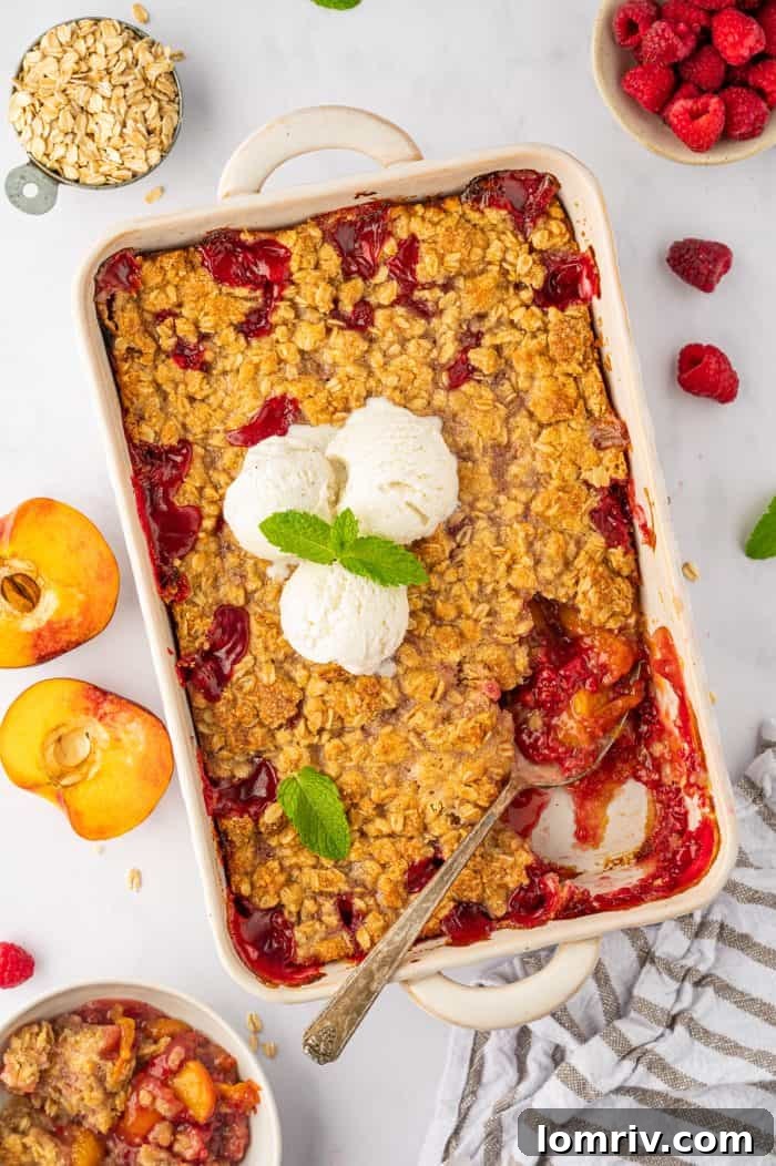 Close-up of a warm peach raspberry crumble with a spoon in it, showcasing the vibrant fruit filling and golden, crunchy oat topping.