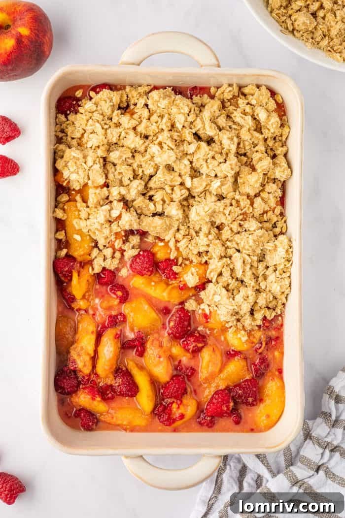 Unbaked peach raspberry crumble completely covered with the oat topping, uniformly spread and ready for the oven.