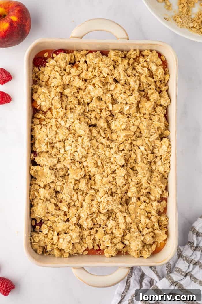 A wider view of the unbaked peach raspberry crumble with the topping evenly spread, sitting in a baking dish before going into the oven.