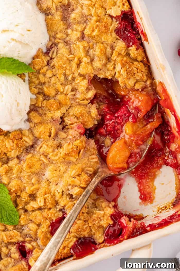 A close-up of a serving of peach raspberry crumble, showing the texture of the fruit and topping, with a spoon digging in, ready to be eaten.