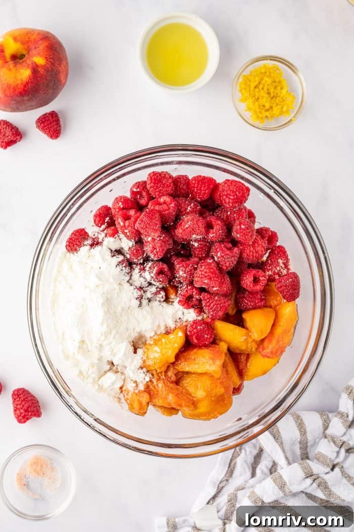 Fresh peach and raspberry filling ingredients, including sugar, cornstarch, and lemon, in a large mixing bowl, ready to be tossed.