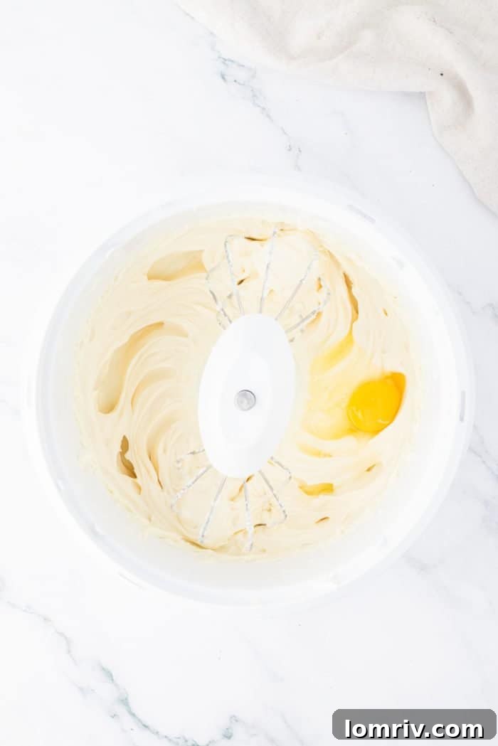 The creamy cheesecake filling being mixed in a large bowl, showcasing its smooth and airy texture before adding eggs and peanut butter.