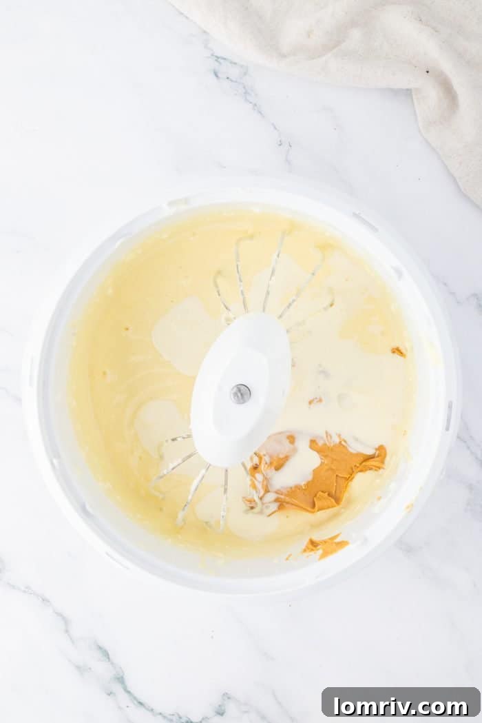 The peanut butter cheesecake filling, now enriched with creamy peanut butter, being gently mixed, creating a rich, uniform color and texture.