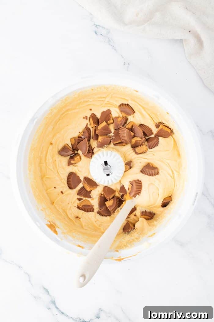 Chopped Reese's Peanut Butter Cups being folded into the smooth peanut butter cheesecake filling, adding delightful texture and flavor bursts.