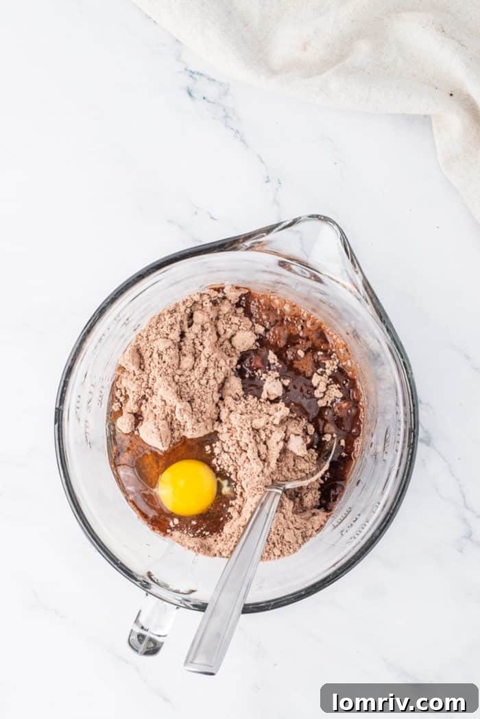 Dry brownie mix ingredients being combined with wet ingredients in a glass mixing bowl, a crucial step for the cheesecake's base.