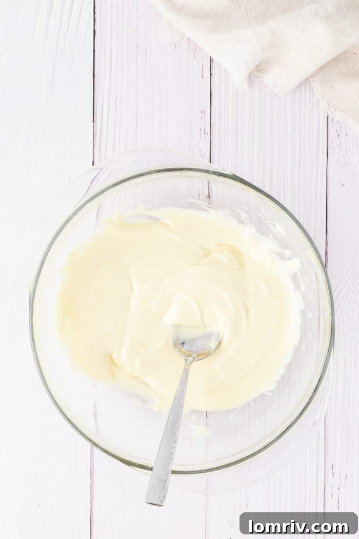 Lustrous melted white chocolate chips gleam in a clear glass bowl, smooth and ready to be incorporated into the cheesecake filling.