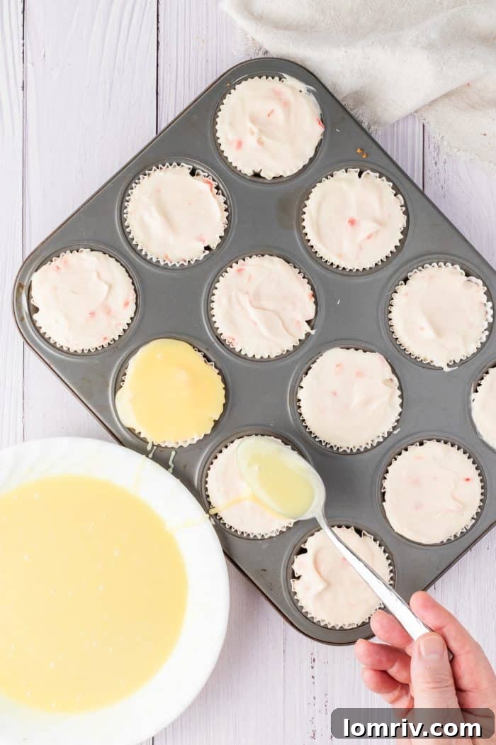 A small spoonful of glistening white chocolate ganache is carefully placed and smoothed over the set cheesecake filling, adding a layer of rich flavor.