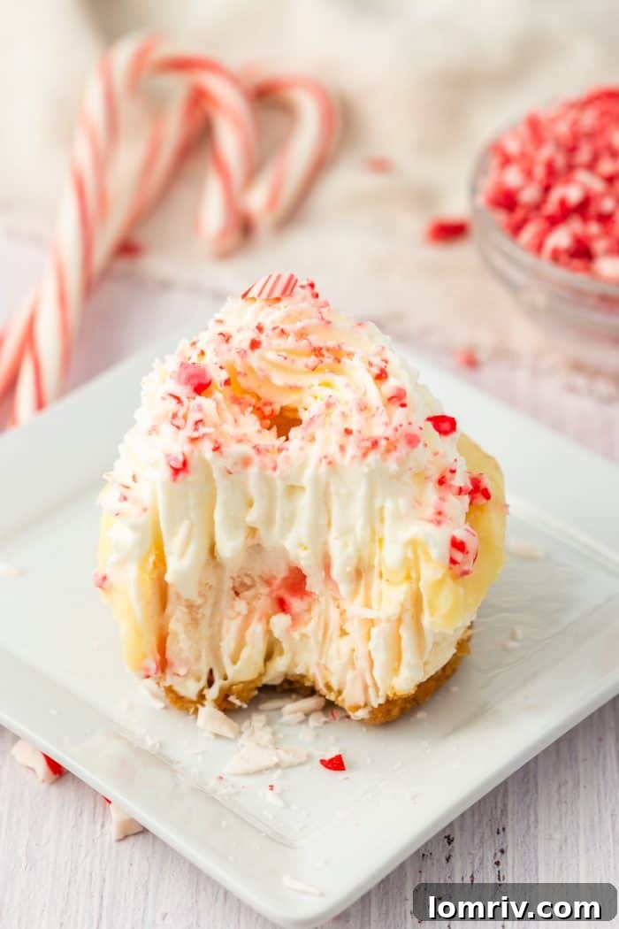 A mini peppermint cheesecake with a perfect bite taken out, resting on a clean square plate, with festive candy canes softly blurred in the background.