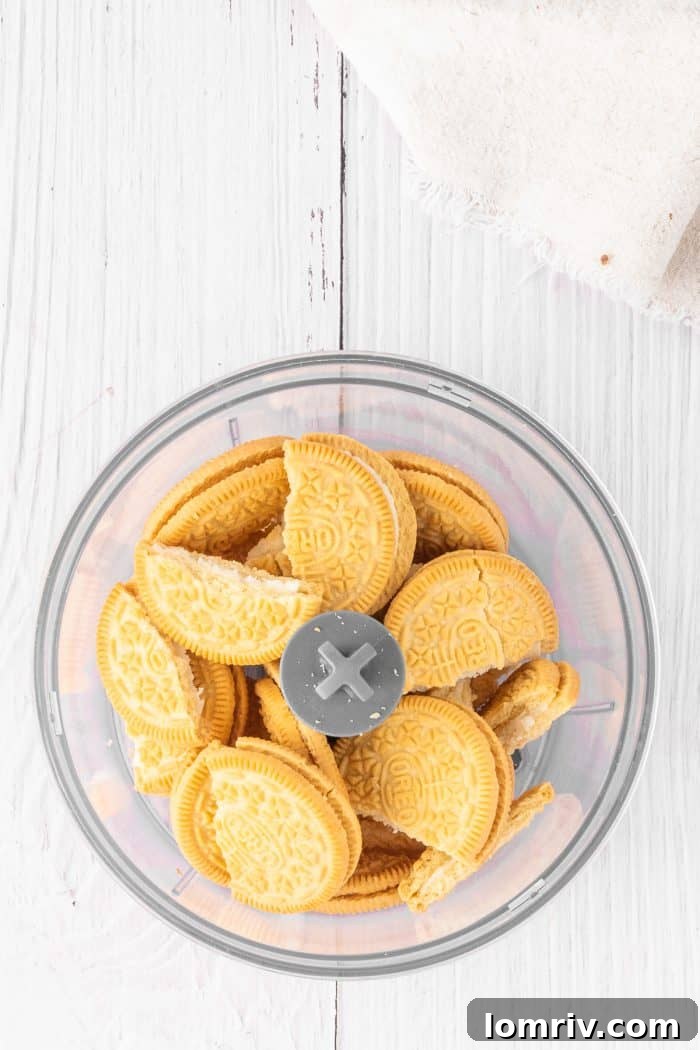 Golden Oreo cookies, perfectly placed inside a food processor, ready to be pulsed into fine crumbs for the cheesecake crust.